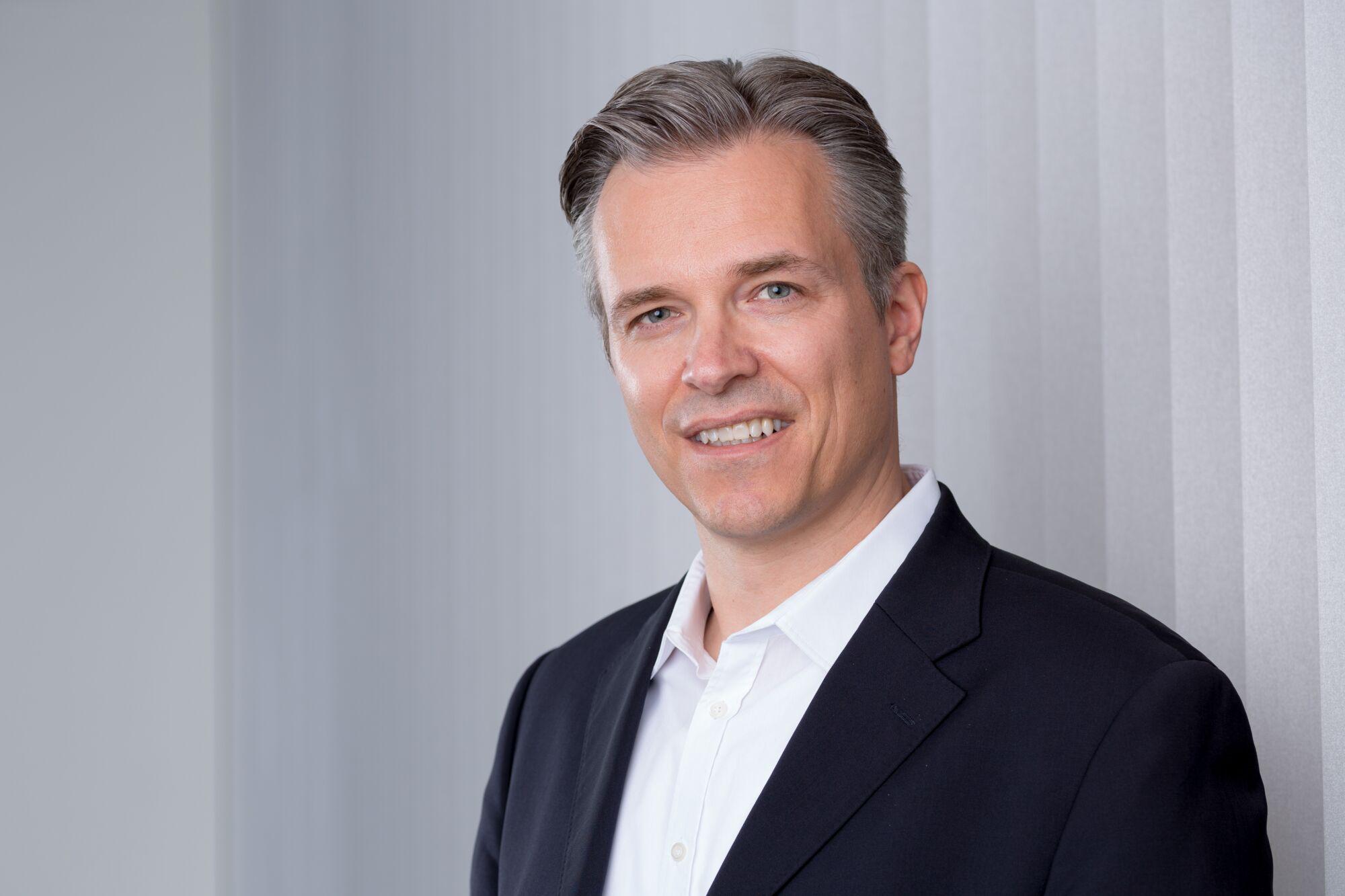 Porträt eines Mannes in schwarzem Anzug und weißem Hemd vor grauem Hintergrund