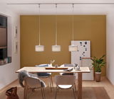 Drie moderne hanglampen met grijze stoffen kappen boven lichte houten eettafel in kamer met gele muur