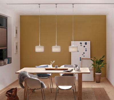 Drie moderne hanglampen met grijze stoffen kappen boven lichte houten eettafel in kamer met gele muur