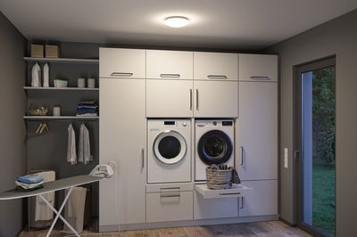 Moderne weiße Einbau-Waschküche mit Waschmaschine, Trockner und integriertem Wäschekorb in Schublade