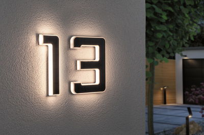 Modern house number 13 in black material with integrated LED lighting on exterior wall.