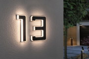 Modern house number 13 in black material with integrated LED lighting on exterior wall.