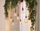Hangende vintage gloeilampen met rode snoeren en groene kerstdecoratie met rode ballen.