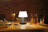 Moderne Tischlampe mit weißem Schirm und schwarzem Sockel auf Holztisch mit Getränken und Karten.