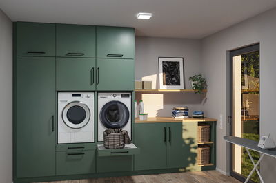 Modern laundry room with green wooden cabinets, washing machine, dryer, and laundry basket.
