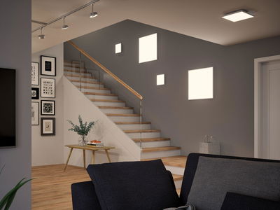 Modern living room with wooden stairs, grey wall, and square LED wall lights for ambient home lighting.