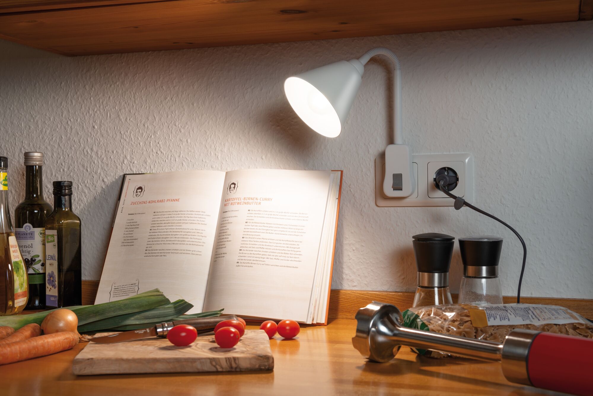 Weiße LED-Leseleuchte mit flexiblem Arm an Küchenwand beleuchtet Kochbuch und frisches Gemüse.