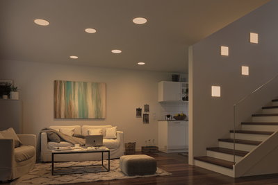 Modern living room with warm white LED ceiling lights and square wall lamps by staircase.