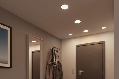 Platte witte LED-inbouwspots in plafond van moderne hal met grijze deur en kapstok