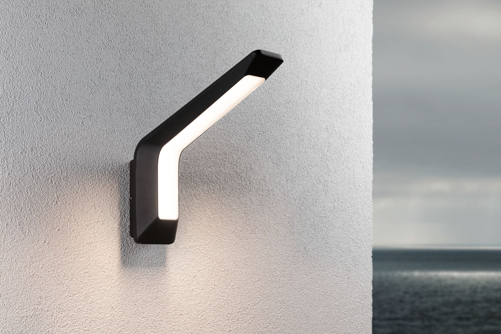 Modern black LED wall light with warm white illumination on white exterior wall by the sea