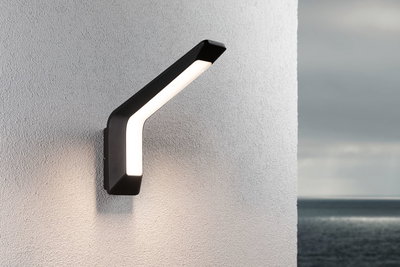 Modern black LED wall light with warm white illumination on white exterior wall by the sea