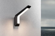 Moderne schwarze LED-Wandleuchte mit warmweißem Licht an weißer Außenwand mit Meerblick