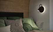 Black LED wall light with flexible reading arm above green bed with cushions in bedroom