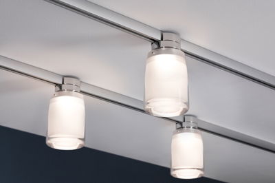 Drei moderne Deckenstrahler mit mattweißem Glas und Chromfassung an Schienensystem für Wohnräume.
