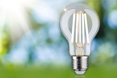 Clear LED light bulb with visible filaments and metal base against green-blue blurred background