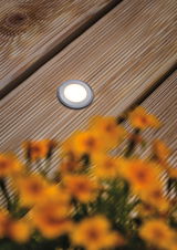 Ronde LED inbouwvloerlicht van geborsteld aluminium op houten terras met bloemen op de voorgrond
