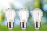 Three clear LED light bulbs with silver base against green-blue background, energy-saving lighting bulbs.