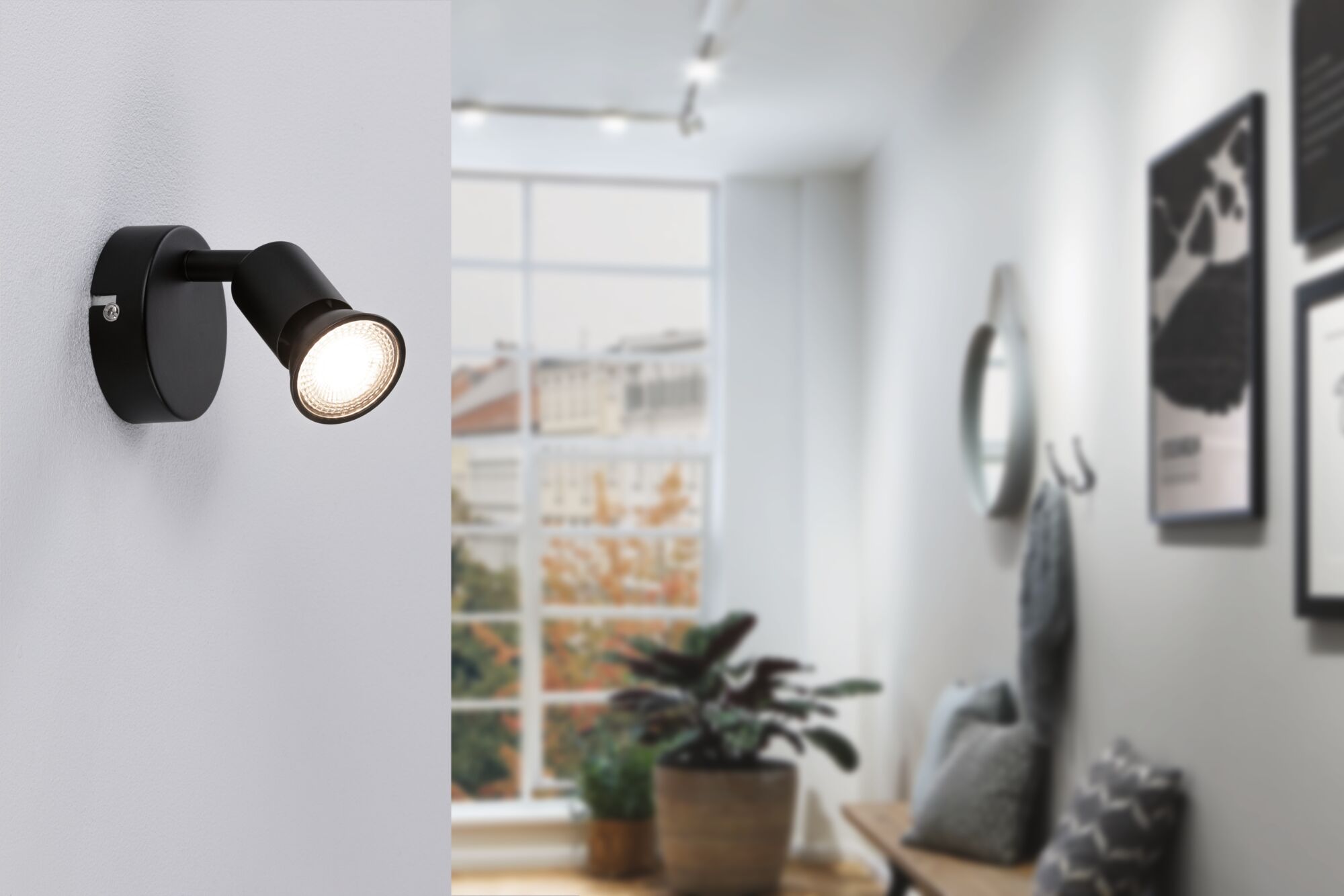 Black metal LED wall spotlight with adjustable head in modern living space with large window.