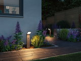 Modern anthracite LED path light with motion sensor illuminating garden path with flower beds.