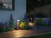 Modern anthracite LED path light with motion sensor illuminating garden path with flower beds.