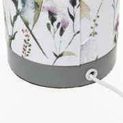Nahaufnahme eines Lampenfußes mit grauem Kunststoff und floral gemustertem Stoffschirm mit Stromkabel