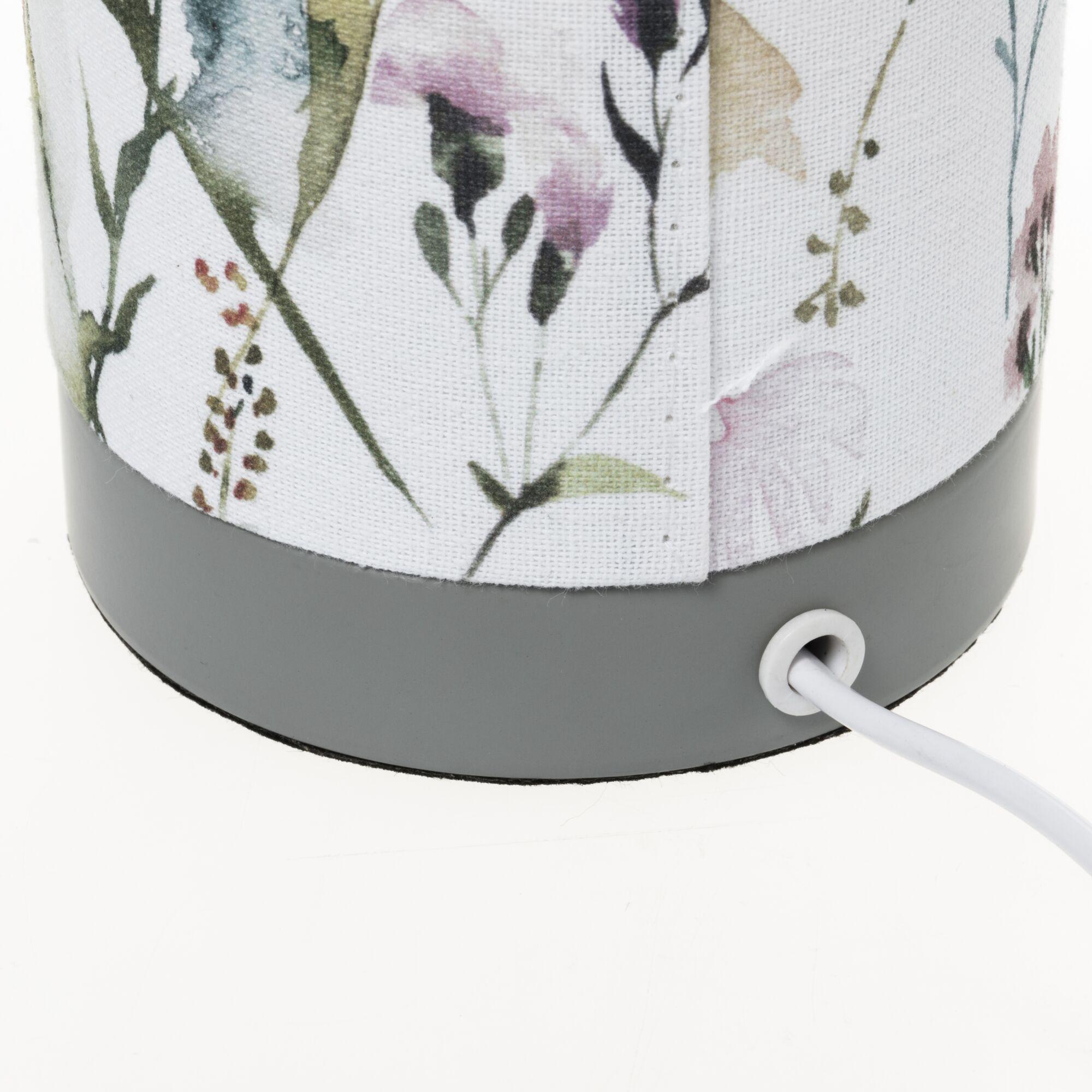 Nahaufnahme eines Lampenfußes mit grauem Kunststoff und floral gemustertem Stoffschirm mit Stromkabel