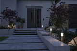 Moderne Außenbeleuchtung mit Edelstahl-Wegeleuchten und warmweißem Licht am Hauseingang mit grauem Beton.