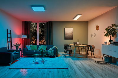 Moderne woonkamer met blauwe en warmwitte LED-plafondlampen, houten vloer en gezellige inrichting