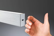 Hand vor schmalem Aluminium-LED-Wandleuchter in Silber mit warmweißem Licht für moderne Innenräume