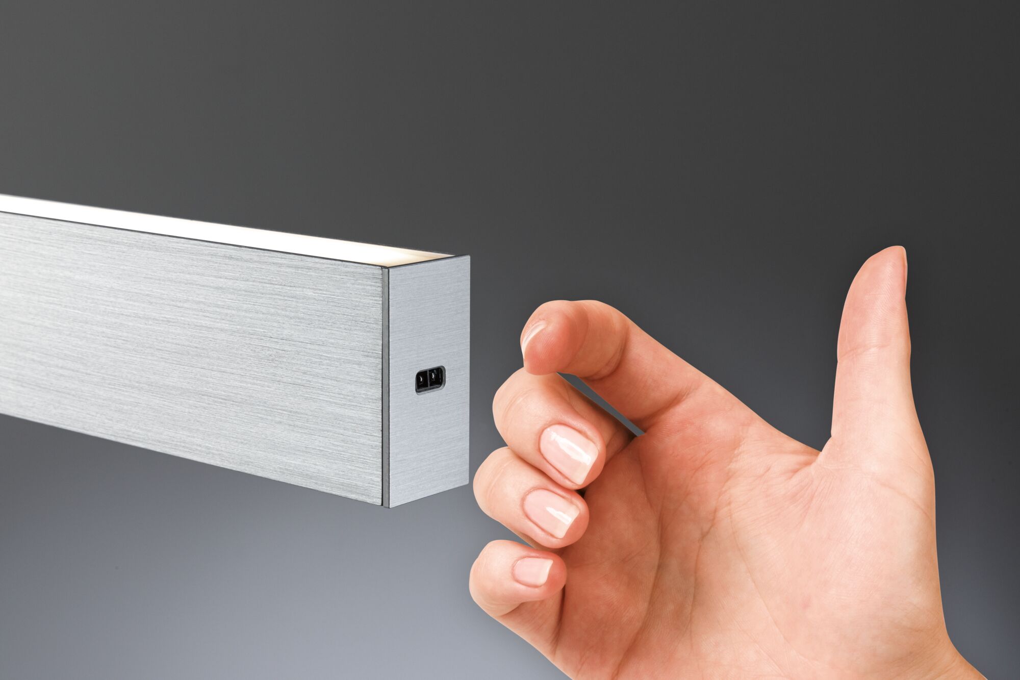 Hand vor schmalem Aluminium-LED-Wandleuchter in Silber mit warmweißem Licht für moderne Innenräume