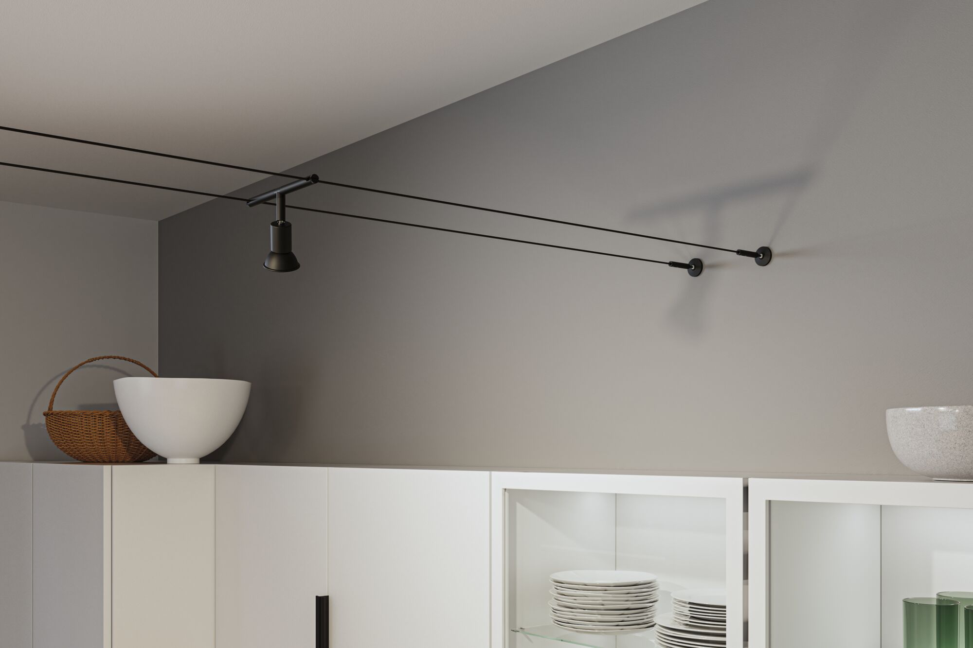 Black cable track ceiling spotlight in modern room above white kitchen cabinet with dishes.