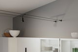 Black cable track ceiling spotlight in modern room above white kitchen cabinet with dishes.