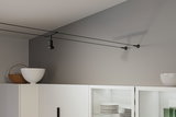 Black cable track ceiling spotlight in modern room above white kitchen cabinet with dishes.