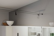 Schwarze Seilzug-Deckenleuchte mit Spot in modernem Raum über weißem Küchenschrank mit Geschirr.