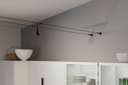 Schwarzes Seil-Lichtsystem mit verstellbarem Spot an grauer Wand über weißem Küchenschrank