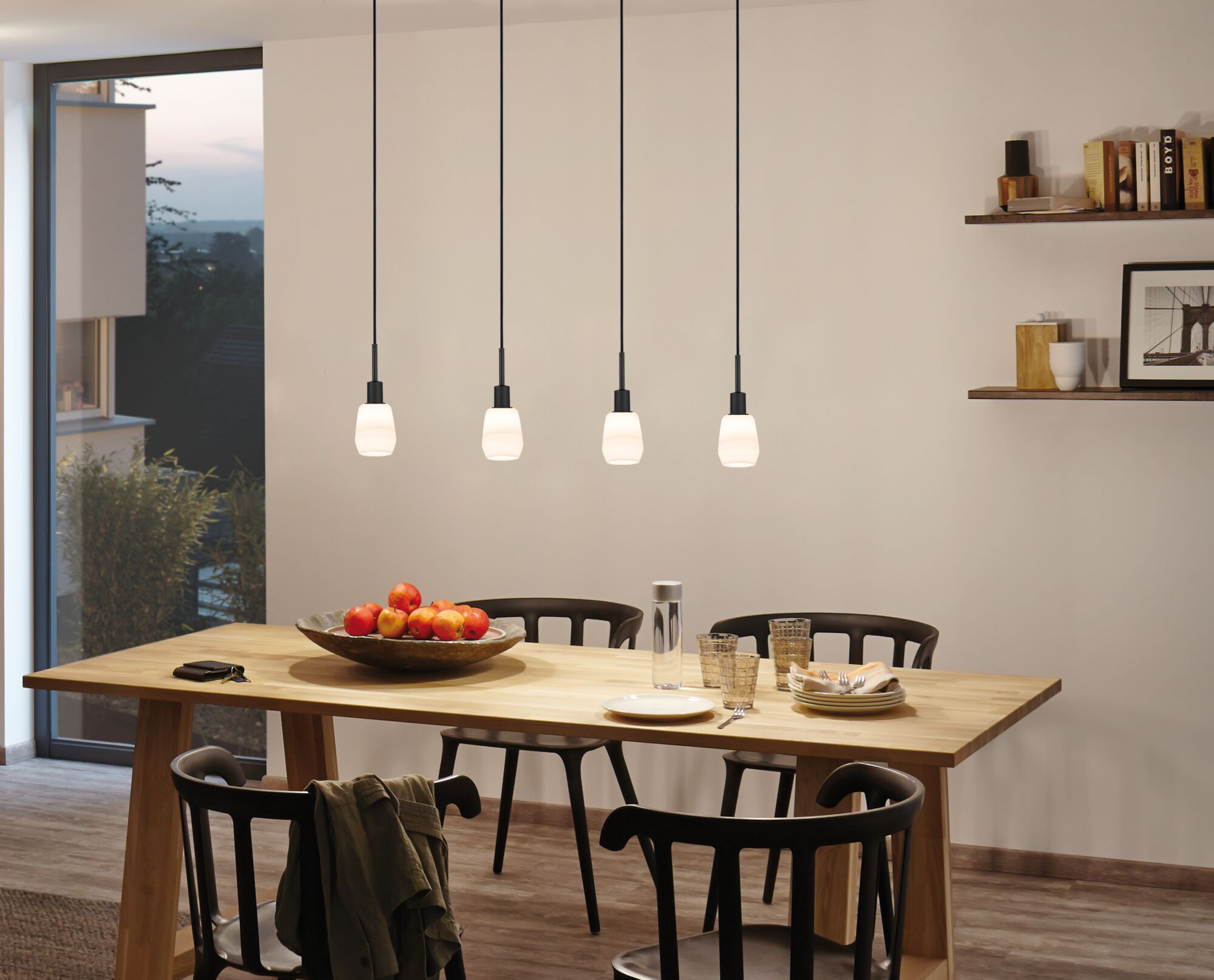 Vier hanglampen met mat wit glas en zwarte snoeren boven houten eettafel