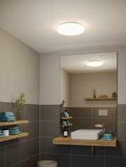 Round white plastic ceiling light in modern bathroom with grey tiles and wooden shelves