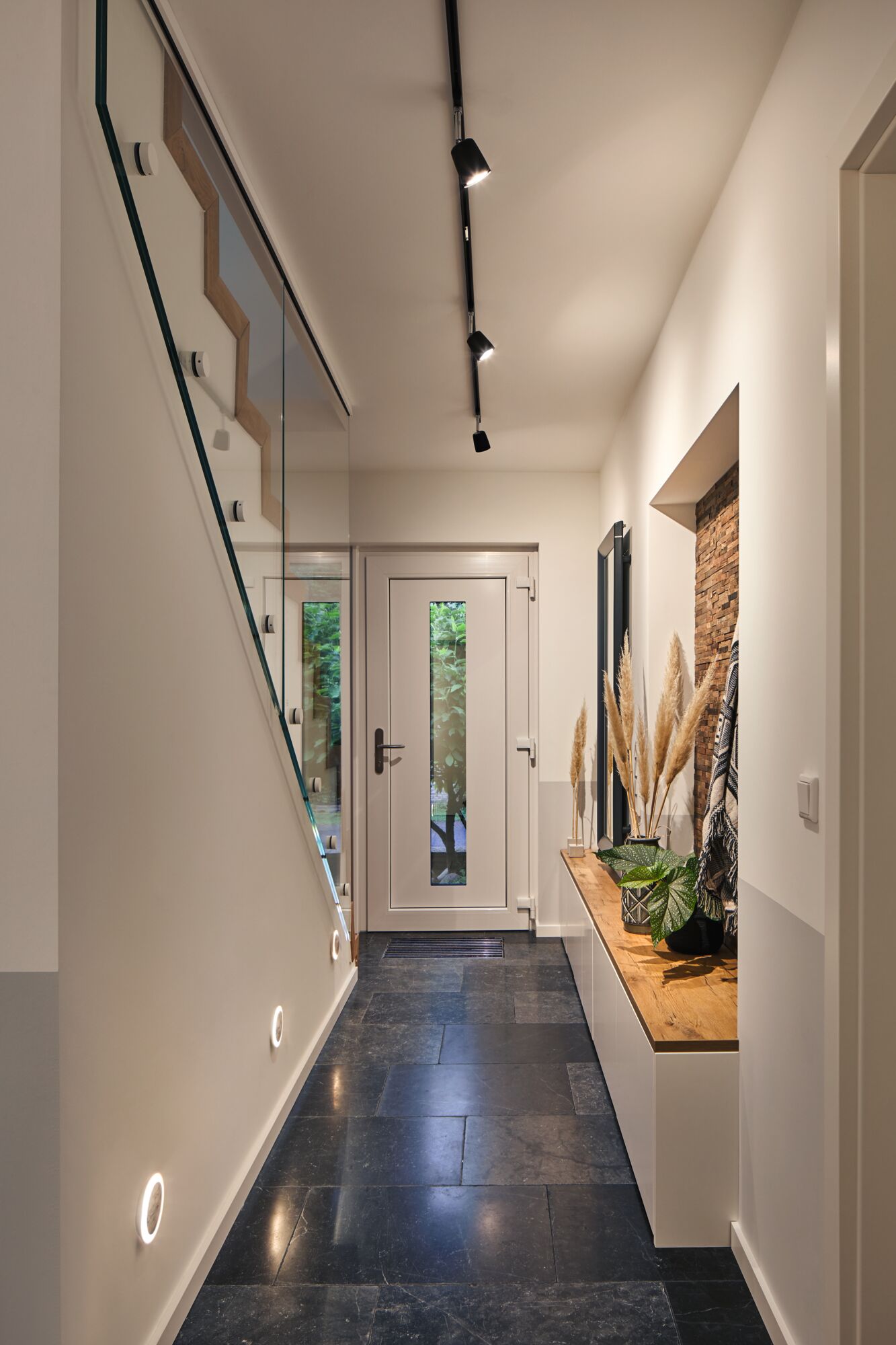 Moderner Flur mit schwarzem Steinboden, weißer Tür, Holzbank und LED-Deckenstrahlern für Wohnraumbeleuchtung