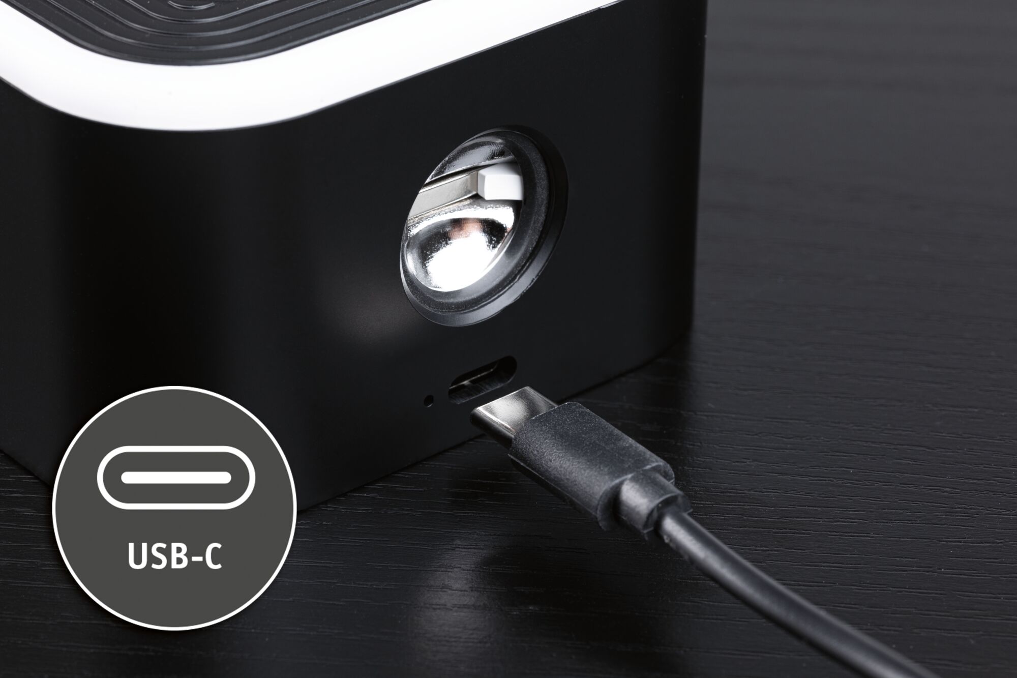 Appareil noir avec port USB-C et câble sur table en bois foncé, gros plan sur la connexion de charge