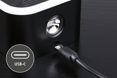 Appareil noir avec port USB-C et câble sur table en bois foncé, gros plan sur la connexion de charge