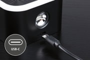 Black device with USB-C port and cable on dark wooden table, close-up of charging connection