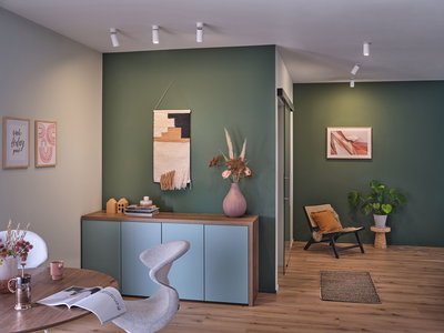 Moderne stue med grøn væg, træskænk, dekorativ vase og stilfulde loftspotter.