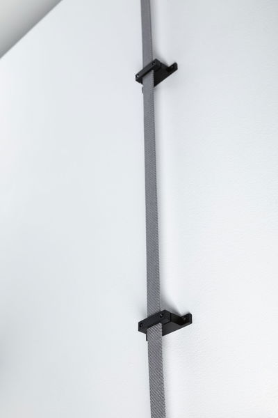 Grey fabric strap with black brackets on white wall for cable management and organization