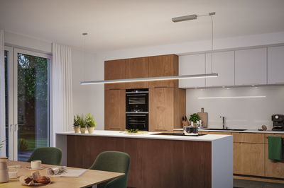 Moderne keuken met houten kasten en wit aanrecht, verlicht door slanke LED-hanglamp