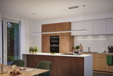 Modern kitchen with wooden cabinets and white countertop, illuminated by slim LED pendant light