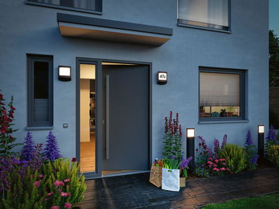 Modern outdoor lighting with black wall and bollard lights at house entrance surrounded by colorful flowers.