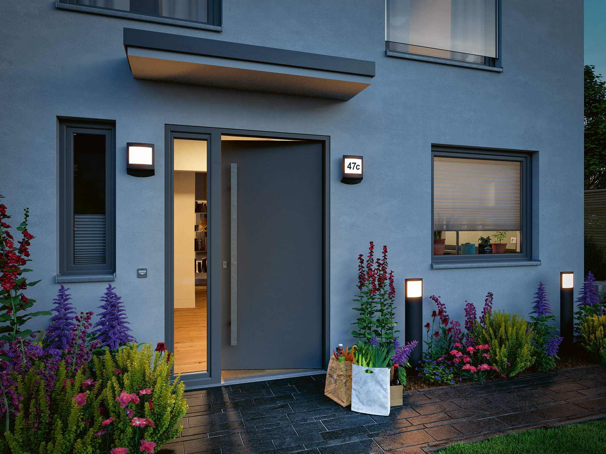 Moderne udendørsbelysning med sorte LED-væglamper og pullerlamper ved grå hoveddør med blomsterbed