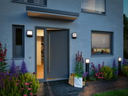 Moderne buitenverlichting met zwarte LED-wandlampen en paaltjes bij grijze voordeur met bloembed
