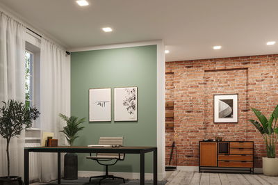 Moderne kantoorruimte met groene accentmuur, zwart bureau, grijze stoel en bakstenen muur met houten kast