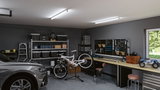 Moderne Garage mit grauem Auto, weißem Mountainbike auf Ständer und Werkbank mit Werkzeugwand.